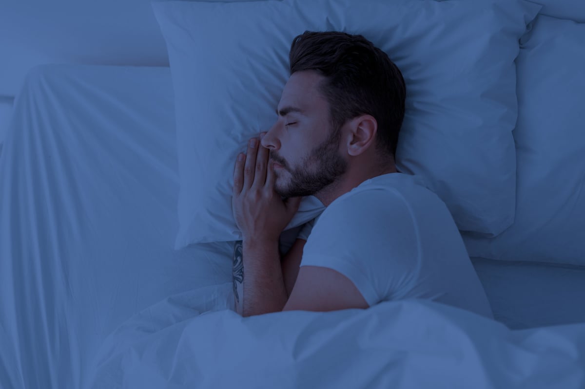 Healthy sleeping, sleep hygiene concept. Young man sleeping in comfy bed at home, copy space, top view. Millennial guy having nap, resting in white cozy bedroom