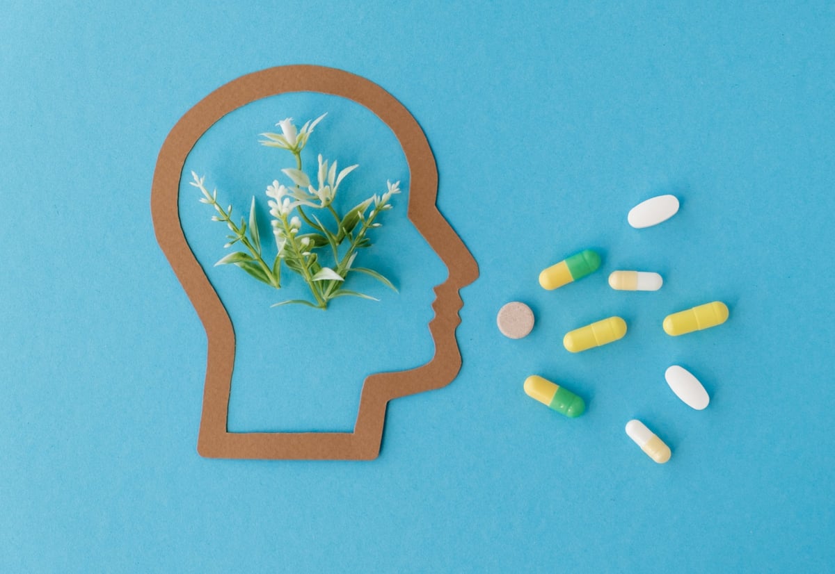 A head with flowers in it is surrounded by pills. The pills are in various colors and sizes, and the flowers are in the shape of a head. Concept of taking care of one's mental health